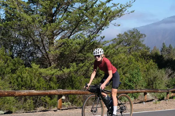 Yolda bisiklet süren bir kadın bisikletçi. Tırmanışa saldırıyor. Çaba gerektiren bisiklet havası. Güzel bir doğada döngü. Bisiklet seti ve kask takan bir kadın bisikletçi. Tenerife, Kanarya Adası, İspanya.