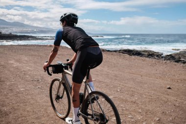 Bisikletçi adam çakıl bisikleti sürüyor. Tenerife, Kanarya Adaları, İspanya 'da Atlantik Okyanusu manzaralı çakıl yolu. Spor motivasyonu. İspanya 'da bisiklet eğitimi. Bisiklet macerası.