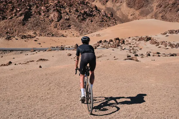 Cyclist practicing on gravel road. Fit man cyclist riding a gravel bike on gravel road with a view of the Teide volcano on Tenerife, Canary Island,  Spain. Cycling gravel adventure. Effort mood.