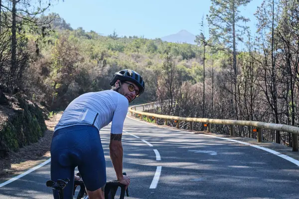 Erkek bisikletçi asfalt yolda Tenerife, Kanarya Adaları, İspanya 'daki yanmış ormandan geçiyor. Spor motivasyonu. İspanya 'da bisiklet eğitimi. Bisiklet macerası. Sporcu bisikletle sıkı çalışıyor.