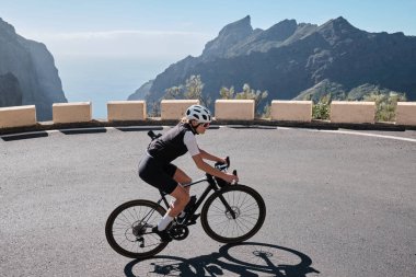 Masca Tenerife 'deki virajlı dağ yolunda bir kadın bisikletçinin görüntüsü. Güzel bir doğada döngü. Spor giyim ve kask takan formda bir sporcu. Spor motivasyon imajı. Tenerife 'de Bisiklet, Kanarya Adaları.