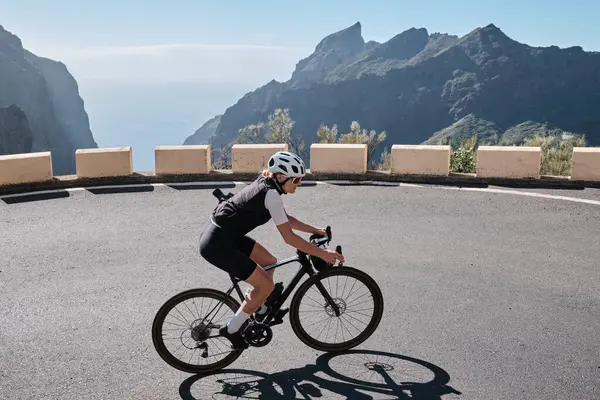 Masca Tenerife 'deki virajlı dağ yolunda bir kadın bisikletçinin görüntüsü. Güzel bir doğada döngü. Spor giyim ve kask takan formda bir sporcu. Spor motivasyon imajı. Tenerife 'de Bisiklet, Kanarya Adaları.