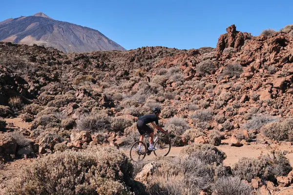 Cyclist practicing on gravel road. Fit man cyclist riding a gravel bike on gravel road with a view of the Teide volcano on Tenerife Canary Island,  Spain. Cycling gravel adventure. Effort mood.