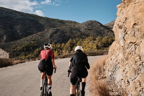 Güneşli bir yaz gününde çakıllı bir yolda çakıllı bisiklet süren iki profesyonel kadın bisikletçi. Doğal kırsalda grup bisikleti sürüşü. Çakıl gelişimi. Çakıl bisikleti macerası. Alicante, İspanya .