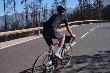 Male cyclist riding on asphalt road through burned forest on Tenerife, Canary Islands, Spain. Sport motivation. Cycling training outdoors in Spain. Cycling adventure . clipart