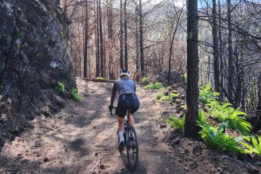 Çakıl yolu üzerinde bisiklet ve kaskla bisiklet süren genç bir kadın bisikletçi. Güzel dağ yollarında bisiklet macerası. Tatil sırasında kırsalda bisiklet süren bir sporcu. İspanya