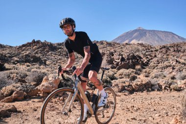 Çakıl yolunda çalışan bir bisikletçi. Taş yolda çakıl bisikleti süren formda bir bisikletçi Tenerife, Kanarya Adası, İspanya 'daki Teide volkanı manzaralı. Bisikletli çakıl macerası. Efor havası.