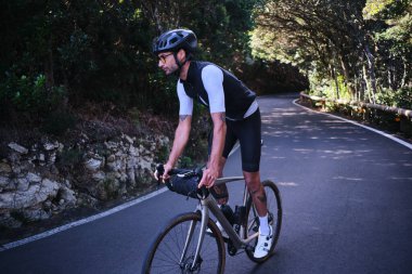 Anaga Park 'ta asfalt orman yolunda bisiklet süren bir erkek bisikletçi var. Tenerife, Kanarya Adaları. Çaba gerektiren bisiklet havası. Güzel bir doğada döngü. Bisiklet seti ve kask takan bir bisikletçi. İspanya