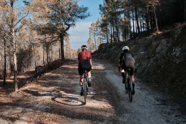 Güneşli bir yaz gününde çakıllı bir yolda çakıllı bisiklet süren iki profesyonel kadın bisikletçi. Doğal kırsalda grup bisikleti sürüşü. Çakıl gelişimi. Çakıl bisikleti macerası. Alicante, İspanya .