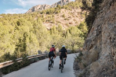 Güneşli bir yaz gününde çakıllı bir yolda çakıllı bisiklet süren iki profesyonel kadın bisikletçi. Doğal kırsalda grup bisikleti sürüşü. Çakıl gelişimi. Çakıl bisikleti macerası. Alicante, İspanya .