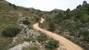Kadın bisikletçi İspanyol dağlarında çakıllı köy yolunda antrenman yapıyor. Kadın bisikleti. Aktif spor. Bisiklet maceraları. Offroad bisikleti. Çakıl yolunda bisiklet süren bir motosiklet..