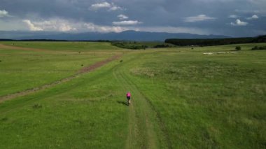 Dağ ve yeşil tarlalarla çevrili inanılmaz destansı bir manzarada bisiklet süren kadın bisikletçiyi takip eden drone. Doğal parktaki asfaltsız yolda çakıl bisikleti sürüyor. Çakıl bisikleti konsepti.