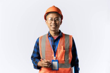 Güvenlik teçhizatı takan Asyalı erkek inşaat işçisi elinde bir dosya, saha müfettişi, endüstriyel ve inşaat konsepti, izole edilmiş beyaz arka plan taşırken kameraya güvenle bakıyor..