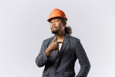 İşaret eden bir patronun mutlu ifadesi. Beyaz arka planda turuncu kasklı takım elbiseli şık Asyalı bir adam. inşaat ya da madencilik sektörü kavramı 