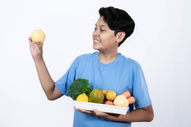Yakışıklı bir Asyalı genç adam elinde armut meyvesi ve bir tepsi meyve ve sebze tutuyor.
