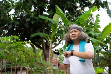 Uzun saçlı bir Asyalı sabah koşusu yaparken bir bardak içki taşıyor.