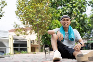 Yorgun adam antrenman yapmak yerine parkta oturup içiyor.