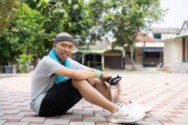 Yorgun adam antrenman yapmak yerine parkta oturup içiyor.