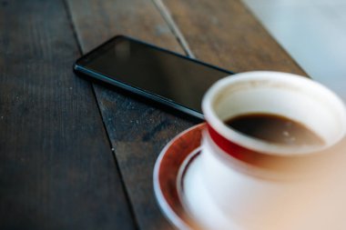 bir fincan sade kahve ve siyah ekranlı bir cep telefonu, reklam ve kopyalama alanı.