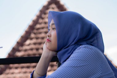 Genç Müslüman kadın tesettürlü, kafede oturmuş meyve suyunun, atıştırmanın ve kahvenin tadını çıkarıyor. Telefon, kırmızı kulaklık, müzik.