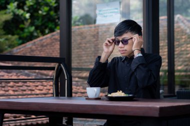 Genç bir adam açık kahve dükkanında ya da kafede kahve içiyor.