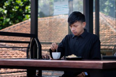 Genç bir adam açık kahve dükkanında ya da kafede kahve içiyor.