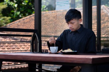 Genç bir adam açık kahve dükkanında ya da kafede kahve içiyor.