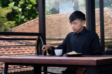 Genç bir adam açık kahve dükkanında ya da kafede kahve içiyor.