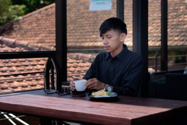 Genç bir adam açık kahve dükkanında ya da kafede kahve içiyor.