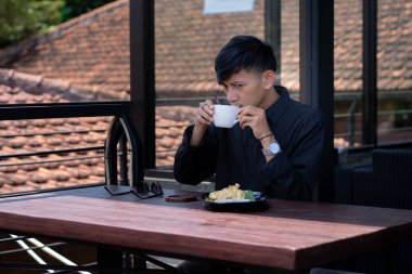 Genç bir adam açık kahve dükkanında ya da kafede kahve içiyor.