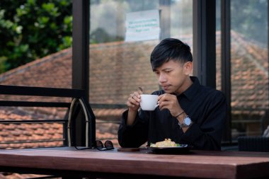 Genç bir adam açık kahve dükkanında ya da kafede kahve içiyor.