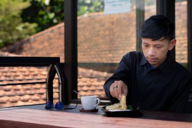 Genç bir adam açık kahve dükkanında ya da kafede kahve içiyor.