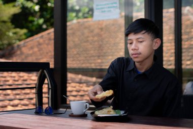 Genç bir adam açık kahve dükkanında ya da kafede kahve içiyor.