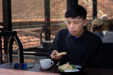 Genç bir adam açık kahve dükkanında ya da kafede kahve içiyor.