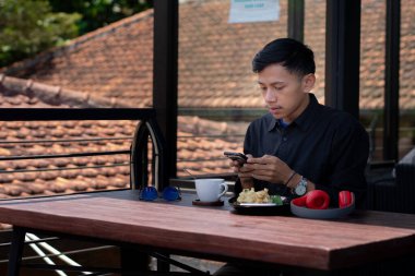 Genç bir adam açık kahve dükkanında ya da kafede kahve içiyor.