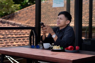 Genç bir adam açık kahve dükkanında ya da kafede kahve içiyor.