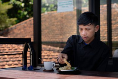 Genç bir adam açık kahve dükkanında ya da kafede kahve içiyor.