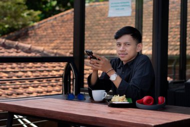 Genç bir adam açık kahve dükkanında ya da kafede kahve içiyor.