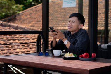 Genç bir adam açık kahve dükkanında ya da kafede kahve içiyor.