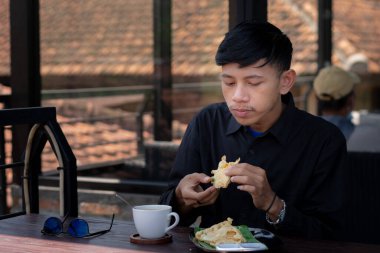 Genç bir adam açık kahve dükkanında ya da kafede kahve içiyor.