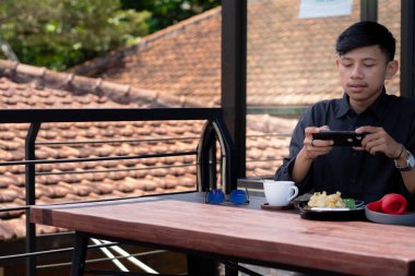 Genç bir adam açık kahve dükkanında ya da kafede kahve içiyor.