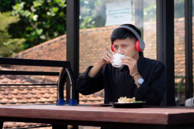 Genç bir adam açık kahve dükkanında ya da kafede kahve içiyor.