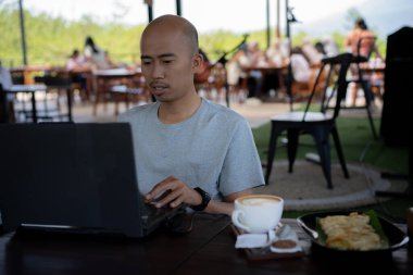 Yarı açık kafede çalışan dizüstü bilgisayarlı ciddi bir adam.