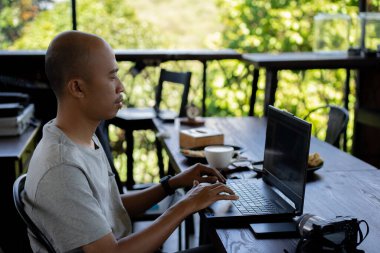 Yarı açık kafede çalışan dizüstü bilgisayarlı ciddi bir adam.