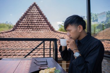 Genç bir Asyalı, kafede bir fincan sıcak kahvenin keyfini çıkarıyor.