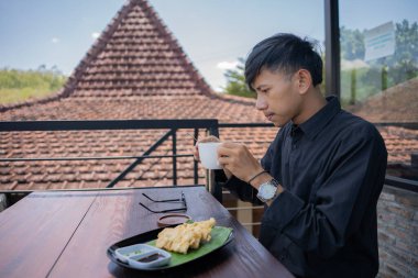 Genç bir Asyalı, kafede bir fincan sıcak kahvenin keyfini çıkarıyor.