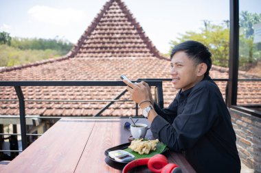 Genç bir adam açık kahve dükkanında ya da kafede kahve içiyor.