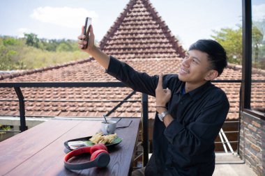 Genç Asyalı bir adam bir kafenin balkonunda rahatlarken selfie çekiyor..