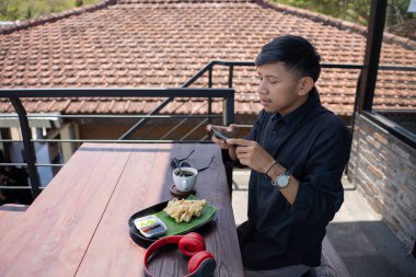 Genç Asyalı bir adam bir kafenin balkonunda dinlenirken seyyar oyun oynuyor..