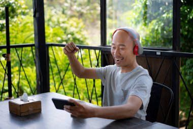 Kel bir Asyalı genç akıllı telefonuyla oyun oynuyor ve bir kafede takılıp dinlenirken mutlu görünüyor..